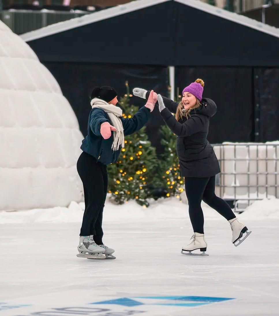 Two women ice skate and give each other a friendly high five.