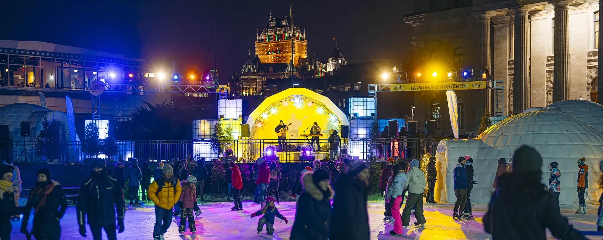 Patineurs sur une patinoire extérieure illuminée, avec un concert en arrière-plan.