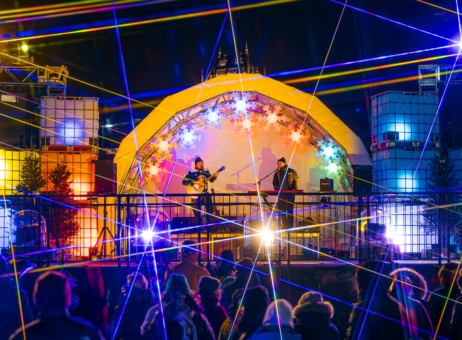 Two musicians on stage under colorful lights and lasers.