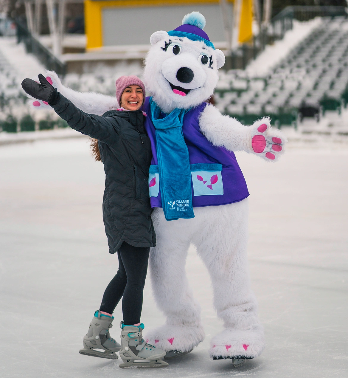 Smiling person posing with a polar bear mascot on the ice rink.