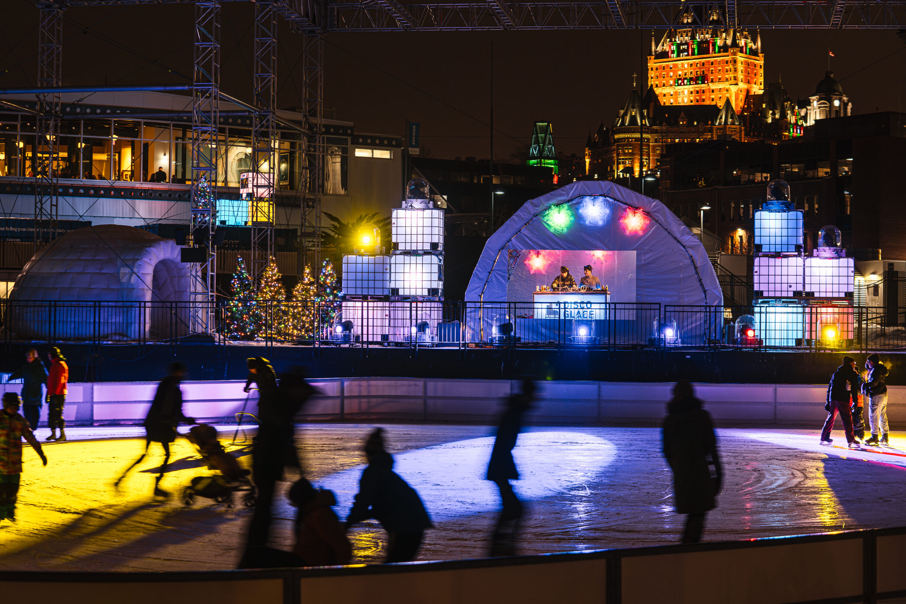 a group of people skating on the ice in front of a dj show at night